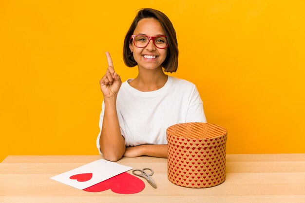 Jonge Spaanse vrouw die een geïsoleerde valentijnskaartgift voorbereidt die nummer één met vinger toont.