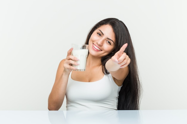 Jonge Spaanse vrouw die een glas melk vrolijke glimlachen houdt richtend aan voorzijde.