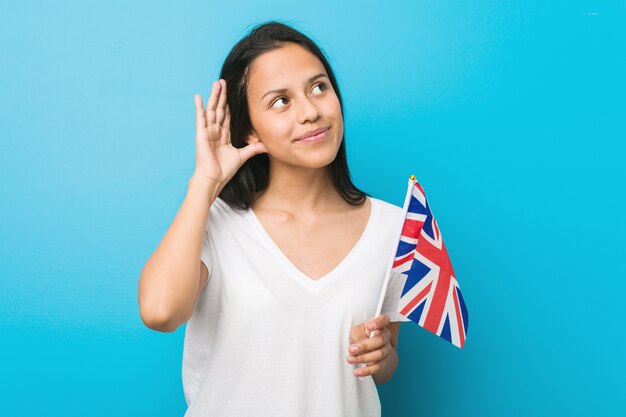 Jonge Spaanse vrouw die een vlag houdt van het Verenigd Koninkrijk die aan een roddel probeert te luisteren.