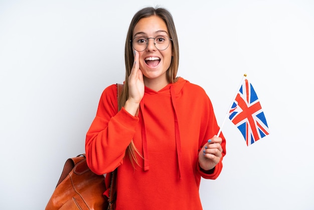 Jonge spaanse vrouw die een vlag van het Verenigd Koninkrijk houdt die op witte achtergrond wordt geïsoleerd die met wijd open mond schreeuwt
