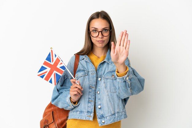 Jonge spaanse vrouw die een vlag van het verenigd koninkrijk houdt over een geïsoleerde witte achtergrond die een stopgebaar maakt