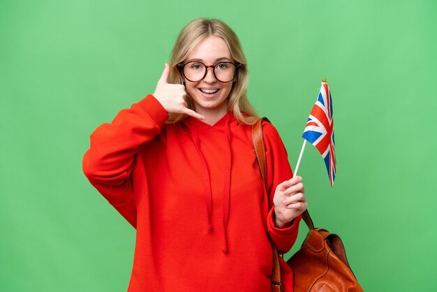 Jonge spaanse vrouw die een vlag van het Verenigd Koninkrijk over een geïsoleerde achtergrond houdt en een telefoongebaar maakt Bel me terug