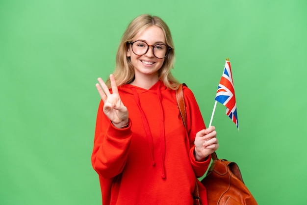 Jonge spaanse vrouw die een vlag van het Verenigd Koninkrijk over een geïsoleerde achtergrond houdt, gelukkig en drie tellen met vingers