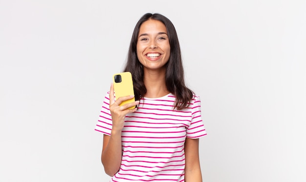 Jonge Spaanse vrouw die er blij en aangenaam verrast uitziet en een smartphone vasthoudt