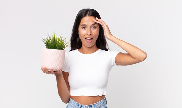 jonge Spaanse vrouw die er blij, verbaasd en verrast uitziet en een decoratieve kamerplant vasthoudt