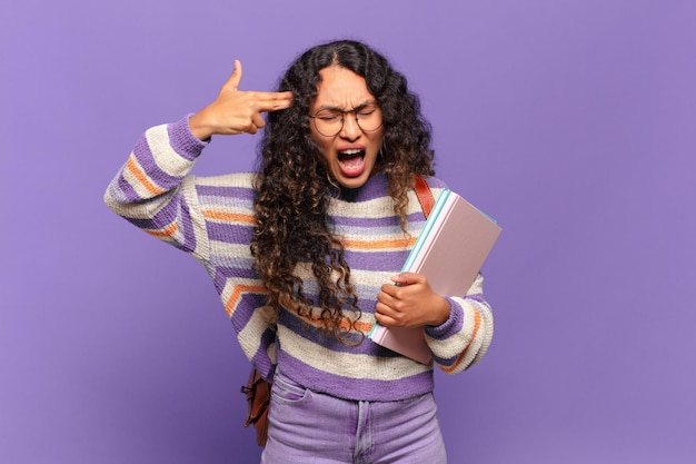 jonge spaanse vrouw die er ongelukkig en gestrest uitziet, zelfmoordgebaar maakt een pistoolteken met de hand, wijzend naar het hoofd. studentenconcept