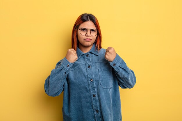 Jonge Spaanse vrouw die er zelfverzekerd, boos, sterk en agressief uitziet, met vuisten klaar om te vechten in bokspositie