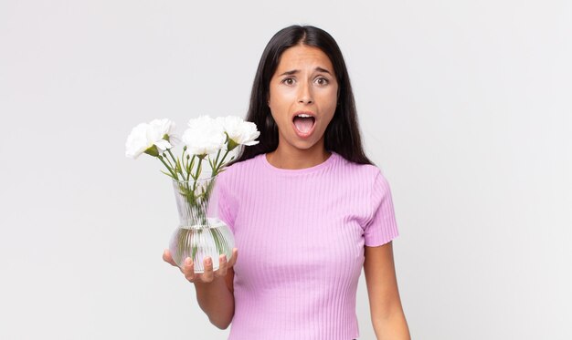 Jonge Spaanse vrouw die erg geschokt of verrast kijkt met decoratieve bloemen