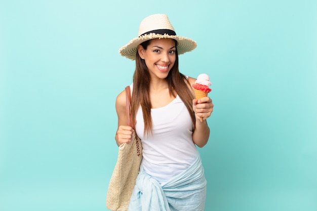 Jonge spaanse vrouw die gelukkig glimlacht met een hand op de heup en zelfverzekerd en een ijsje vasthoudt. zomer concept