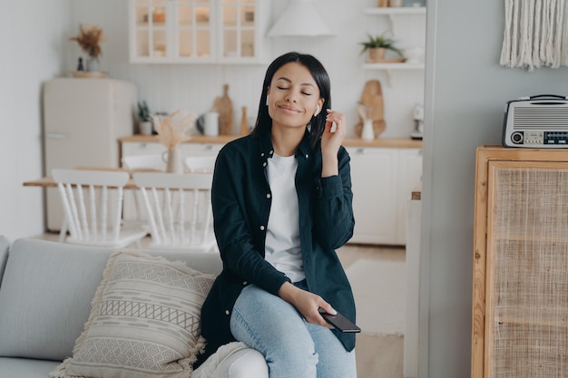 Jonge Spaanse vrouw die geniet van muziek die luistert in airpods die ontspannen met haar ogen dicht