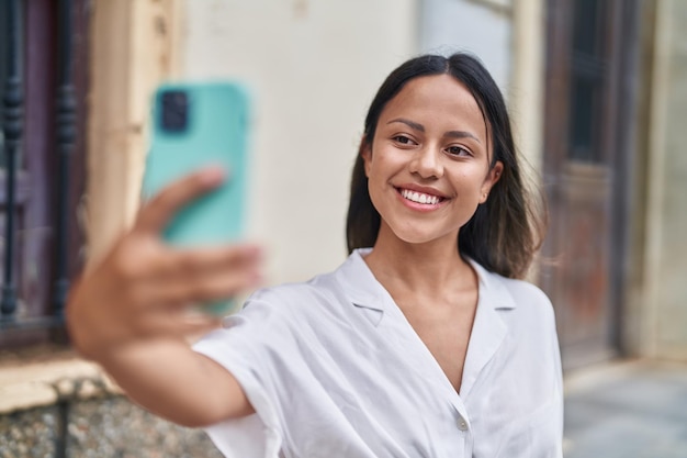 Jonge spaanse vrouw die lacht zelfverzekerd selfie maken door de smartphone op straat