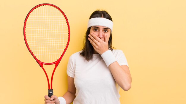 Jonge spaanse vrouw die mond bedekt met handen met een geschokt tennisconcept