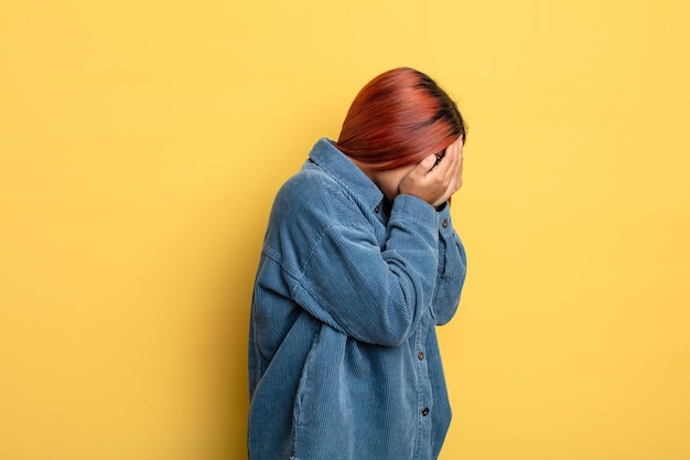 Jonge Spaanse vrouw die ogen bedekt met handen met een droevige, gefrustreerde blik van wanhoop, huilend, zijaanzicht