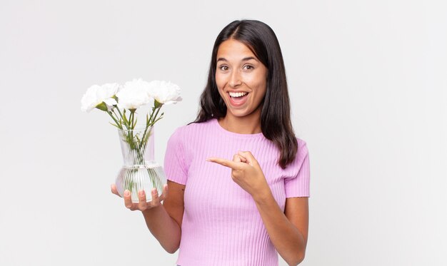 Jonge Spaanse vrouw die opgewonden en verrast kijkt en naar de zijkant wijst met decoratieve bloemen