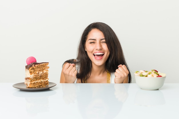 Jonge Spaanse vrouw die tussen cake of fruit kiest die onbezorgd en opgewekt toejuichen.