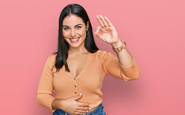 Jonge spaanse vrouw die vrijetijdskleding draagt die positief glimlacht en ok teken doet met hand en vingers. succesvolle uitdrukking.