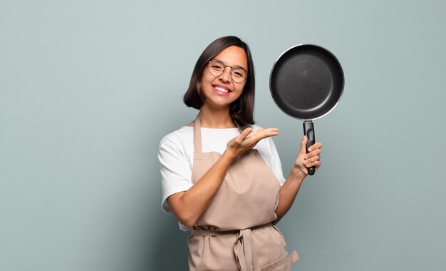 Jonge Spaanse vrouw die vrolijk glimlacht, zich gelukkig voelt en een concept in exemplaarruimte met handpalm toont