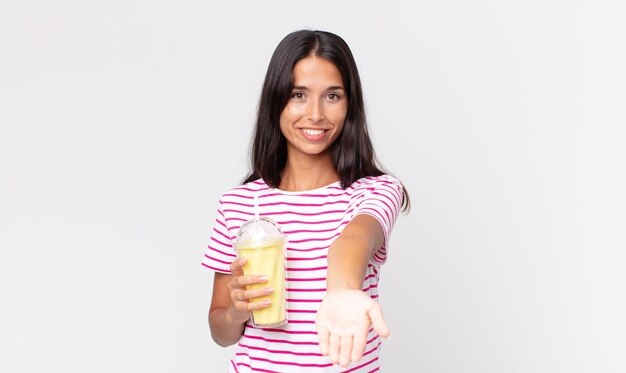 Jonge Spaanse vrouw die vrolijk lacht met vriendelijk en een concept aanbiedt en toont en een vanila smoothy milkshake vasthoudt