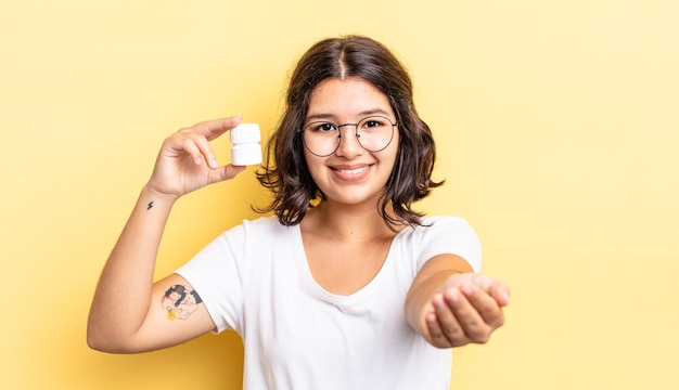 Jonge spaanse vrouw die vrolijk lacht met vriendelijk en een concept aanbiedt en toont. ziekte pillen concept