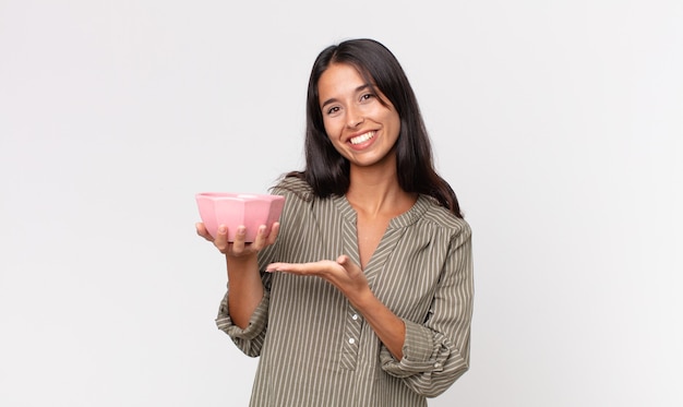 Jonge Spaanse vrouw die vrolijk lacht, zich gelukkig voelt en een concept toont en een lege kom of pot vasthoudt