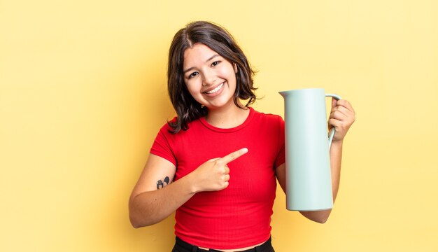 Jonge spaanse vrouw die vrolijk lacht, zich gelukkig voelt en naar de zijkant wijst. thermos concept