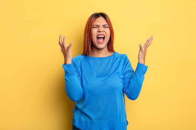 Jonge Spaanse vrouw die woedend schreeuwt, zich gestrest en geïrriteerd voelt met de handen in de lucht en zegt waarom ik?