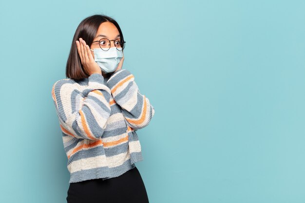 Jonge Spaanse vrouw die zich blij, opgewonden en verrast voelt, opzij kijkt met beide handen op het gezicht