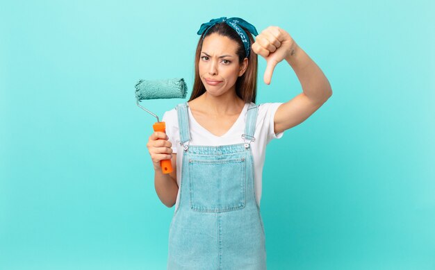 Jonge Spaanse vrouw die zich boos voelt, duimen naar beneden laat zien en een muur schildert