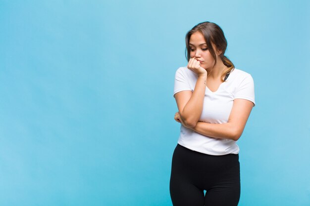 Jonge Spaanse vrouw die zich ernstig, bedachtzaam en bezorgd voelt, zijwaarts staart met de hand tegen de kin gedrukt