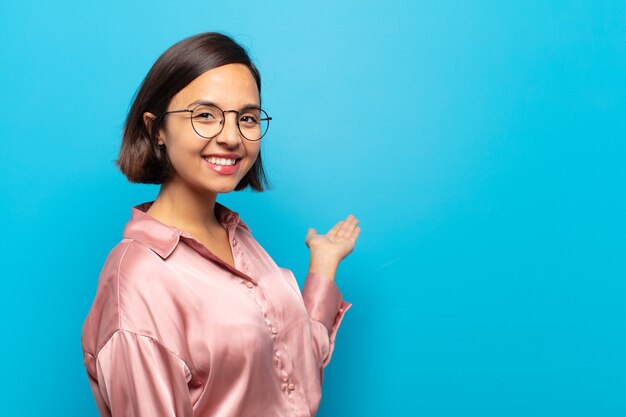 Jonge Spaanse vrouw die zich gelukkig en opgewekt voelt, je glimlacht en verwelkomt, je uitnodigt met een vriendelijk gebaar