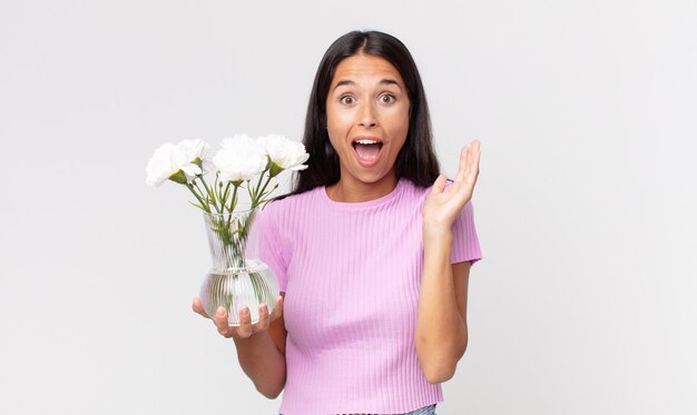 Jonge Spaanse vrouw die zich gelukkig en verbaasd voelt over iets ongelooflijks met decoratieve bloemen