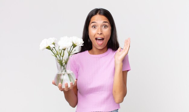 Jonge Spaanse vrouw die zich gelukkig en verbaasd voelt over iets ongelooflijks met decoratieve bloemen