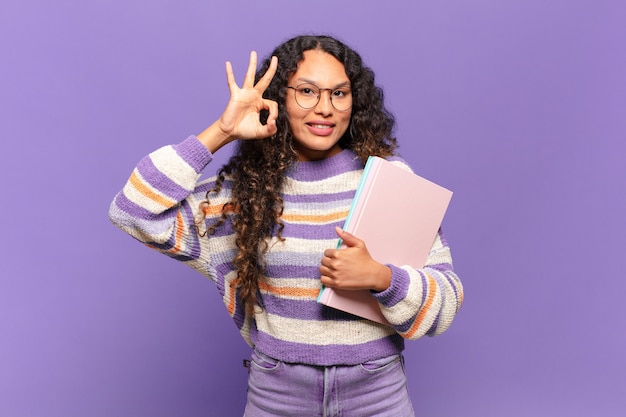 Jonge Spaanse vrouw die zich gelukkig, ontspannen en tevreden voelt, goedkeuring toont met een goed gebaar, glimlachend. student concept