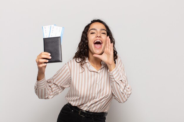 Jonge Spaanse vrouw die zich gelukkig, opgewonden en positief voelt, een grote schreeuw geeft met handen naast de mond, roept