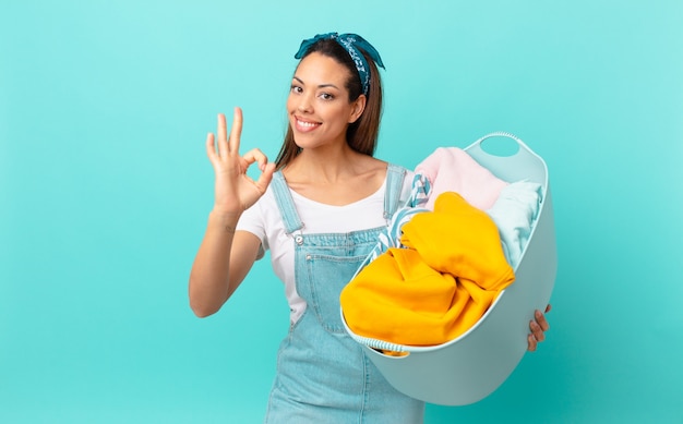 Jonge Spaanse vrouw die zich gelukkig voelt, goedkeuring toont met een goed gebaar en kleren wast