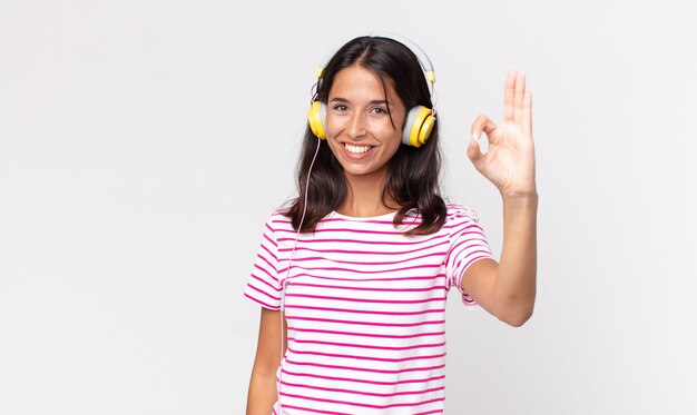 jonge Spaanse vrouw die zich gelukkig voelt, goedkeuring toont met een goed gebaar, muziek luistert met een koptelefoon