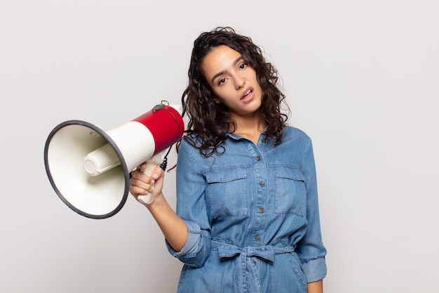 Jonge Spaanse vrouw die zich verbaasd en verward voelt, met een domme, verbijsterde uitdrukking op zoek naar iets onverwachts