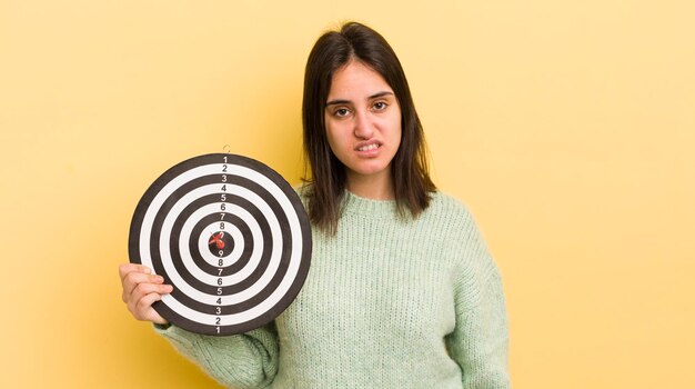 Foto jonge spaanse vrouw die zich verward en verward voelt met het doelconcept van darts