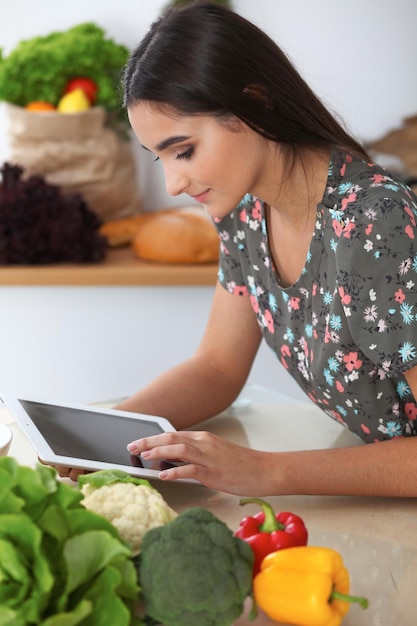 Jonge Spaanse vrouw doet online winkelen met tabletcomputer en creditcard Huisvrouw heeft nieuw recept gevonden om in een keuken te koken