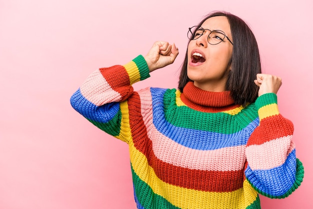 Jonge Spaanse vrouw geïsoleerd op roze achtergrond die vuist opheft na een overwinningswinnaarconcept