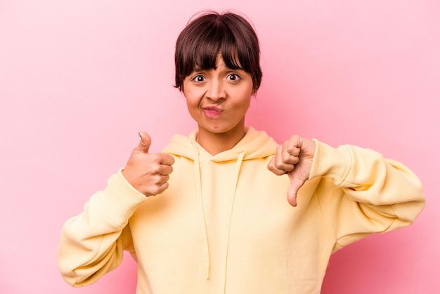 Foto jonge spaanse vrouw geïsoleerd op roze achtergrond met duimen omhoog en duim omlaag moeilijk kiezen concept