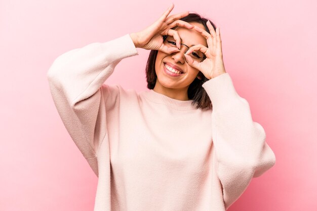 Jonge Spaanse vrouw geïsoleerd op roze achtergrond met goed teken boven de ogen