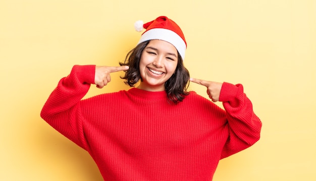 Jonge Spaanse vrouw glimlachend vol vertrouwen wijzend naar eigen brede glimlach. kerst concept
