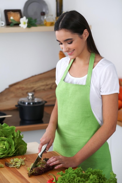 Jonge Spaanse vrouw kookt in de keuken Huisvrouw snijdt groenten en groen vlees voor verse salade