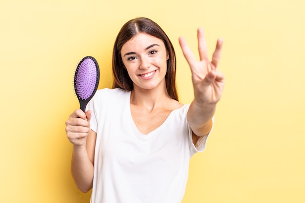 Foto jonge spaanse vrouw lacht en ziet er vriendelijk uit, met nummer drie. haar borstel concept