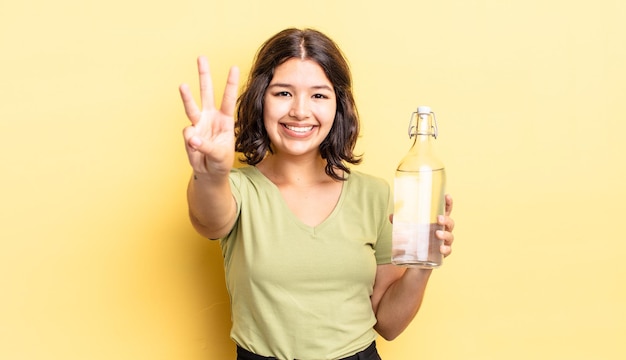 Jonge Spaanse vrouw lacht en ziet er vriendelijk uit, met nummer drie. waterfles concept