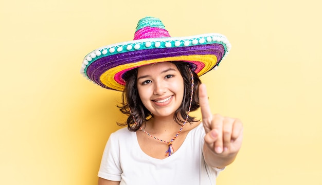 Jonge Spaanse vrouw lacht en ziet er vriendelijk uit, met nummer één. mexicaanse hoed concept