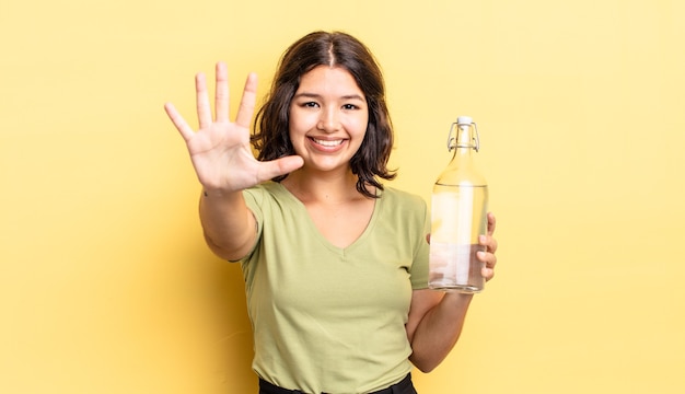 Jonge Spaanse vrouw lacht en ziet er vriendelijk uit, met nummer vijf. waterfles concept