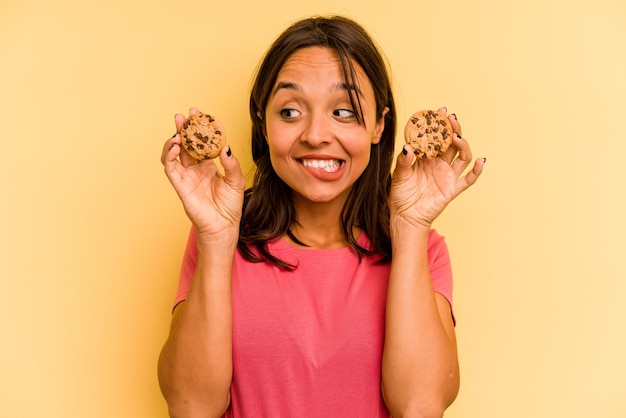 Jonge Spaanse vrouw met cookies geïsoleerd op gele achtergrond