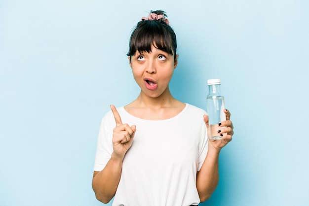 Jonge Spaanse vrouw met een fles water geïsoleerd op een blauwe achtergrond die ondersteboven wijst met geopende mond